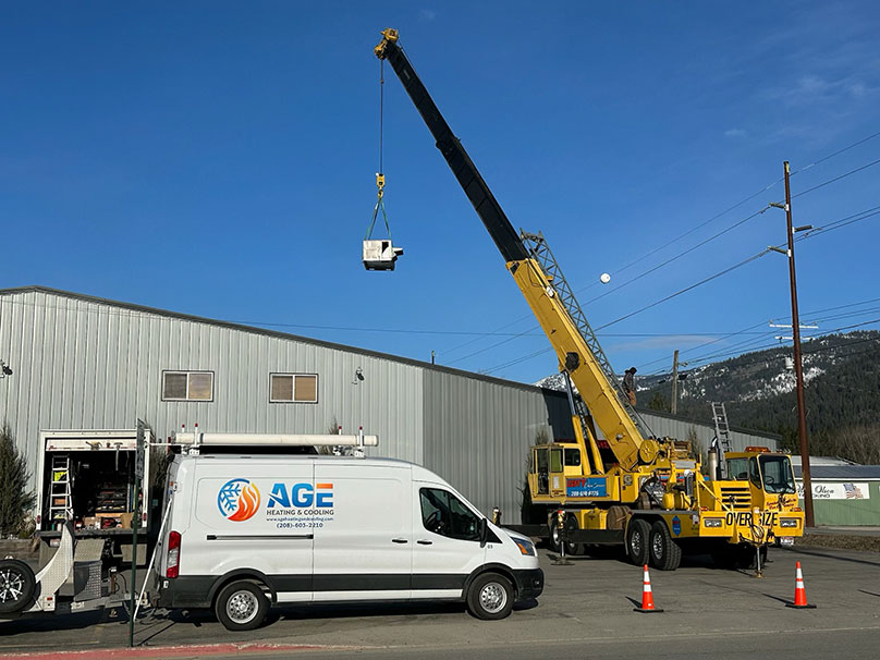 Age van with a crane in the background lifting an air conditioner unit